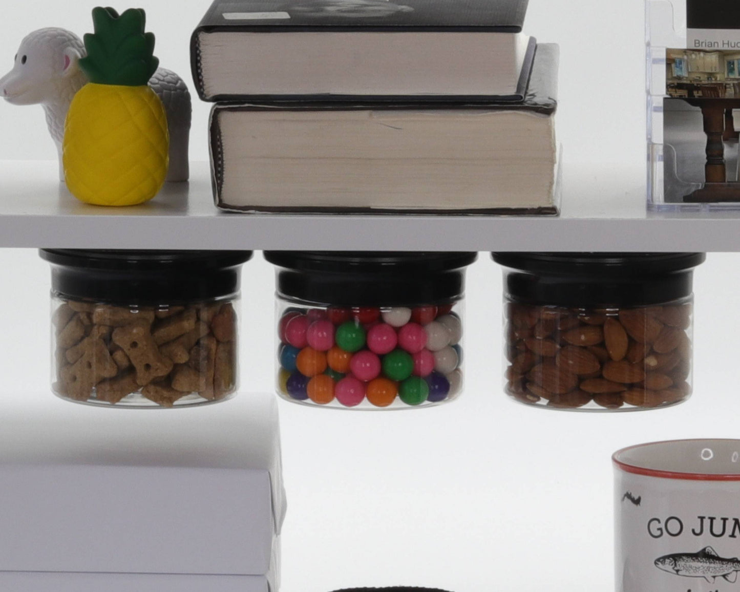 Three stash jars mounted under a shelf storing dog treats, gumballs, and almonds, ideal for kitchen or pantry organization.