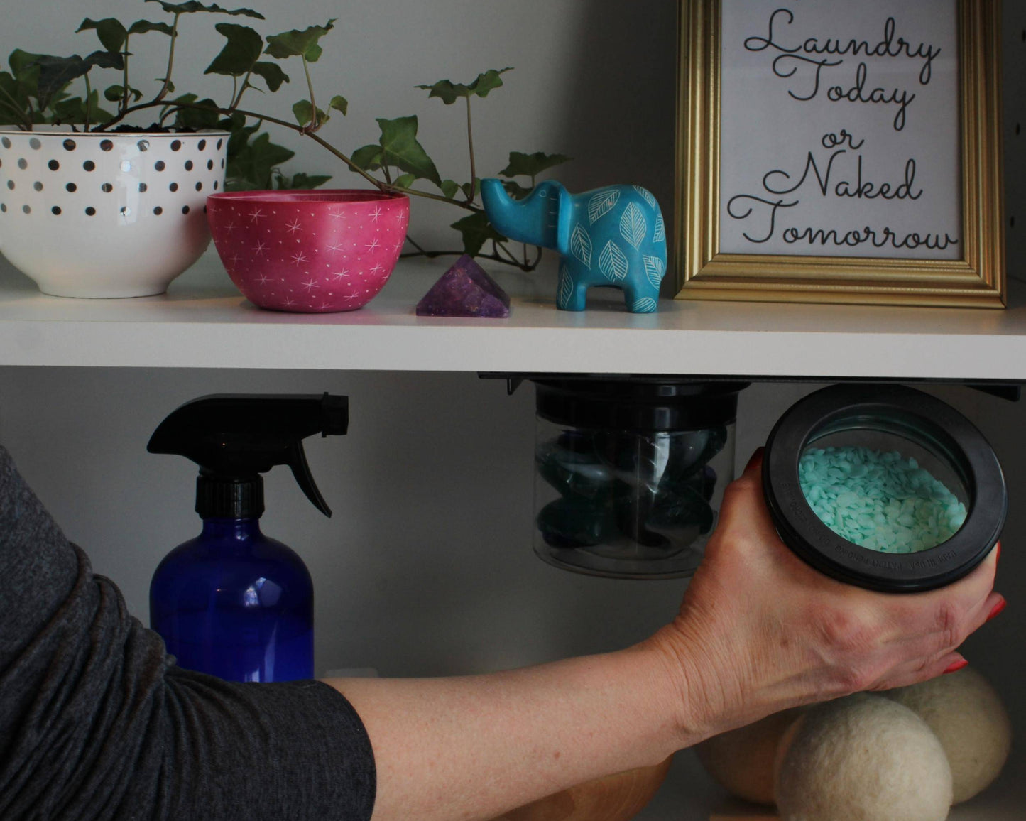 Hand accessing magnetic airtight jar with laundry detergent under shelf, highlighting sustainable and organized laundry storage.