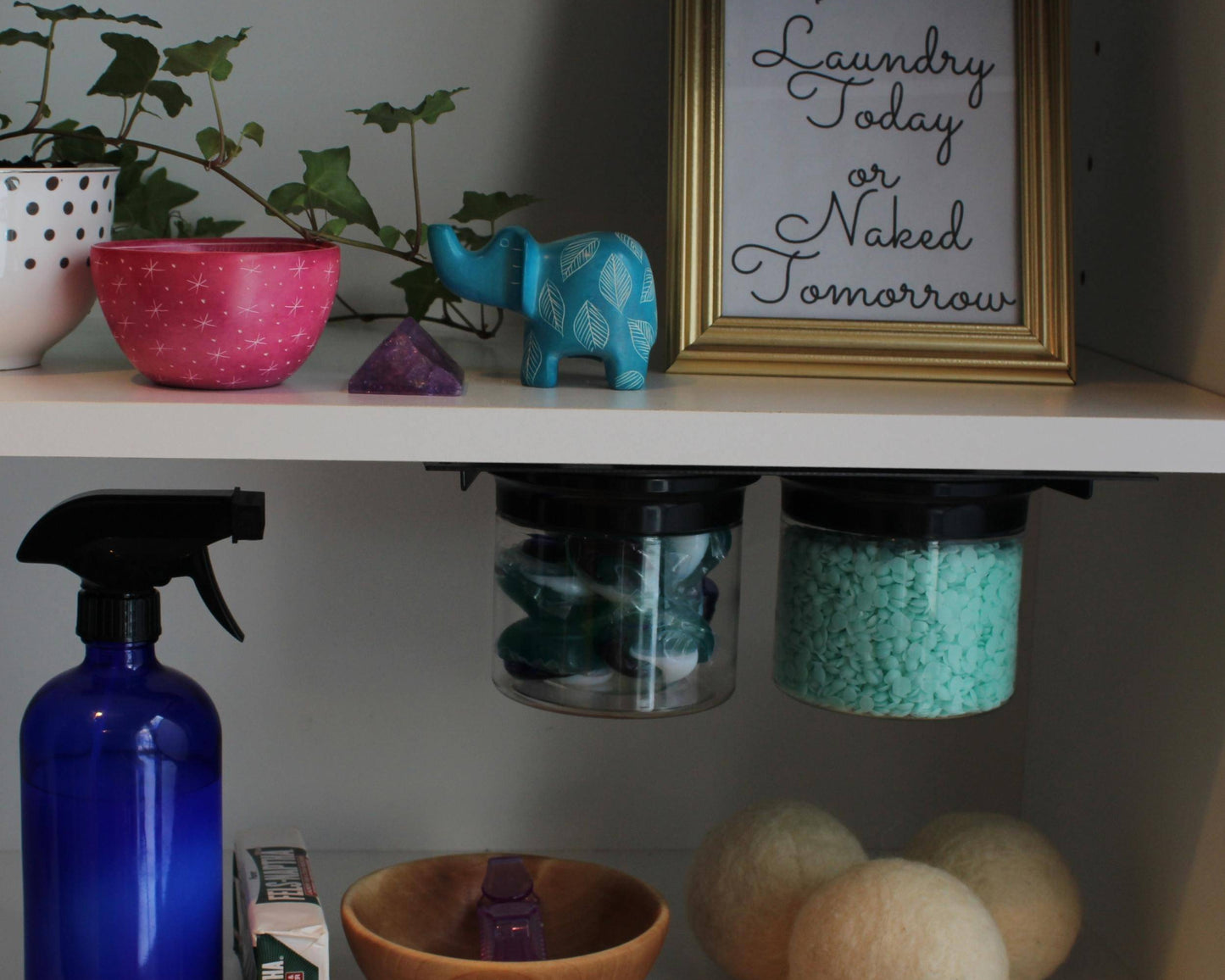 Black-lid airtight jars under laundry shelf storing detergent pods and powder, with eco-friendly laundry items and decor nearby.