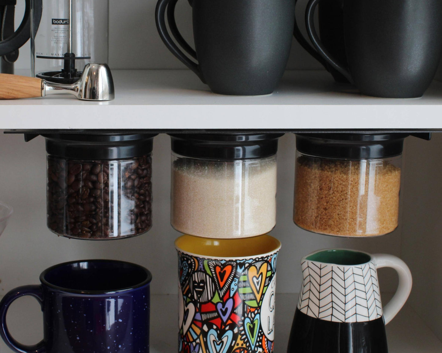 Under cabinet airtight storage jars holding coffee beans, sugar, and brown sugar, maximizing kitchen shelf space with magnetic lids.