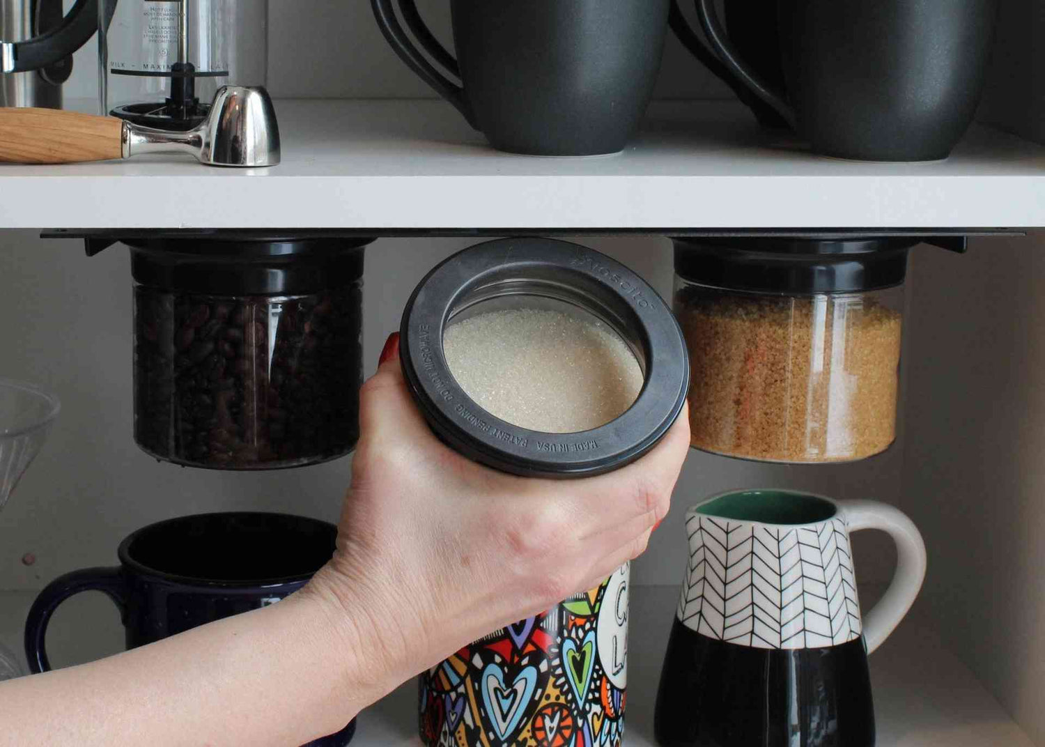 Hand holding airtight jar filled with sugar from under-shelf mount, demonstrating user-friendly and space-saving kitchen storage.