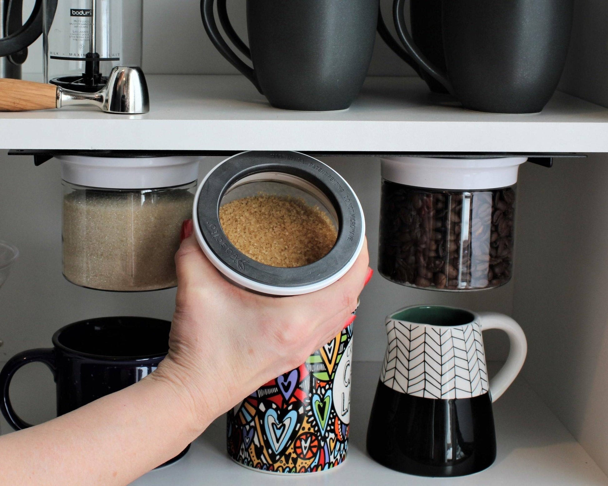 Hand removing brown sugar from a white magnetic airtight jar under a kitchen shelf, showing accessible and space-saving storage.