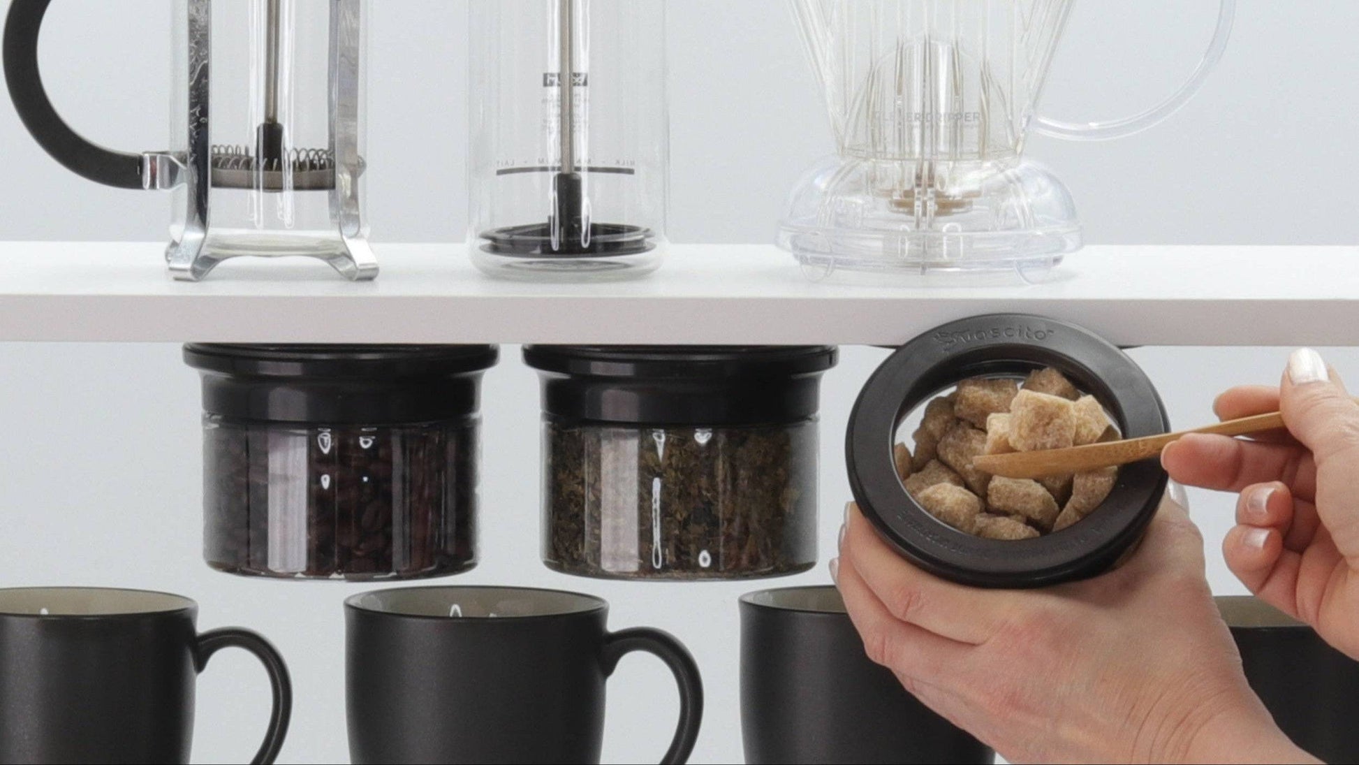 Kitchen Organizer Stash Jars mounted under shelf storing coffee beans, tea, and sugar cubes in airtight containers above mugs.