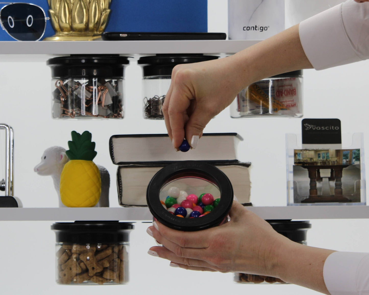 Office Stash Jar - Magnetic Jar in use with person retrieving gumballs, demonstrating fast-access storage under a white shelf.