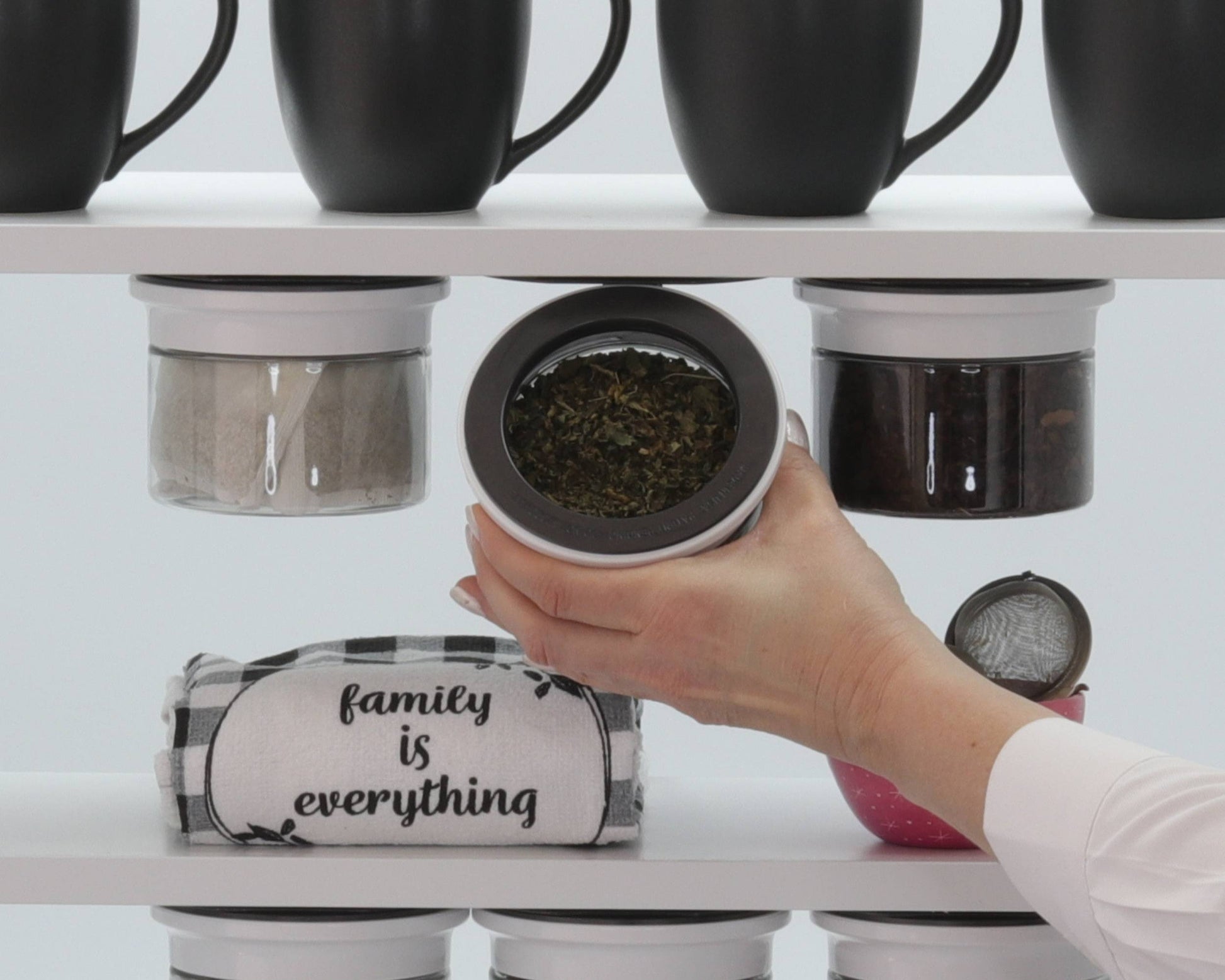 Hand accessing tea leaves from Kitchen Organizer Stash Jar mounted under shelf, surrounded by mugs and kitchen accessories.