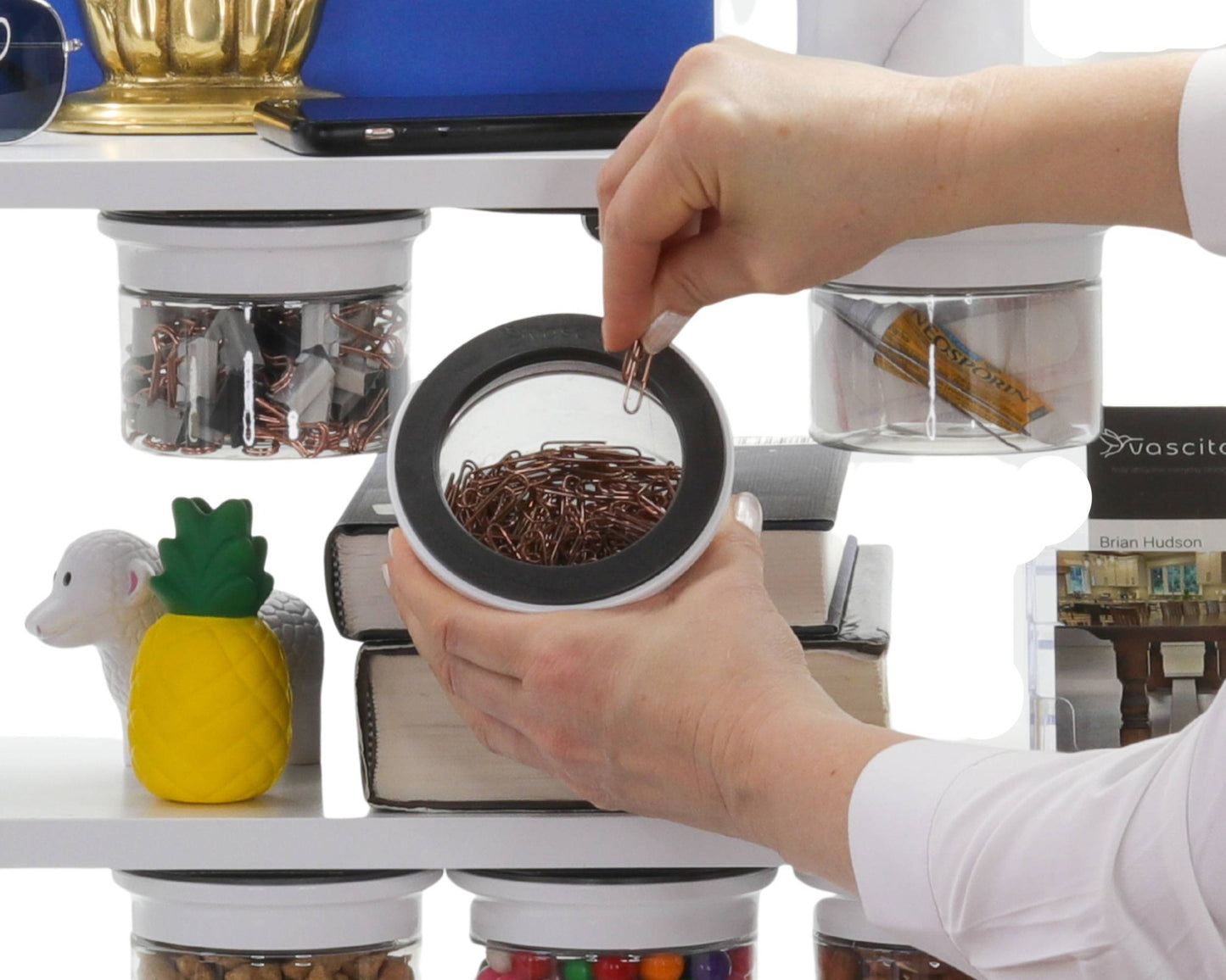 Person removing paperclip from Office Stash Jar - Magnetic Jar under a shelf, surrounded by books and decorative office items.