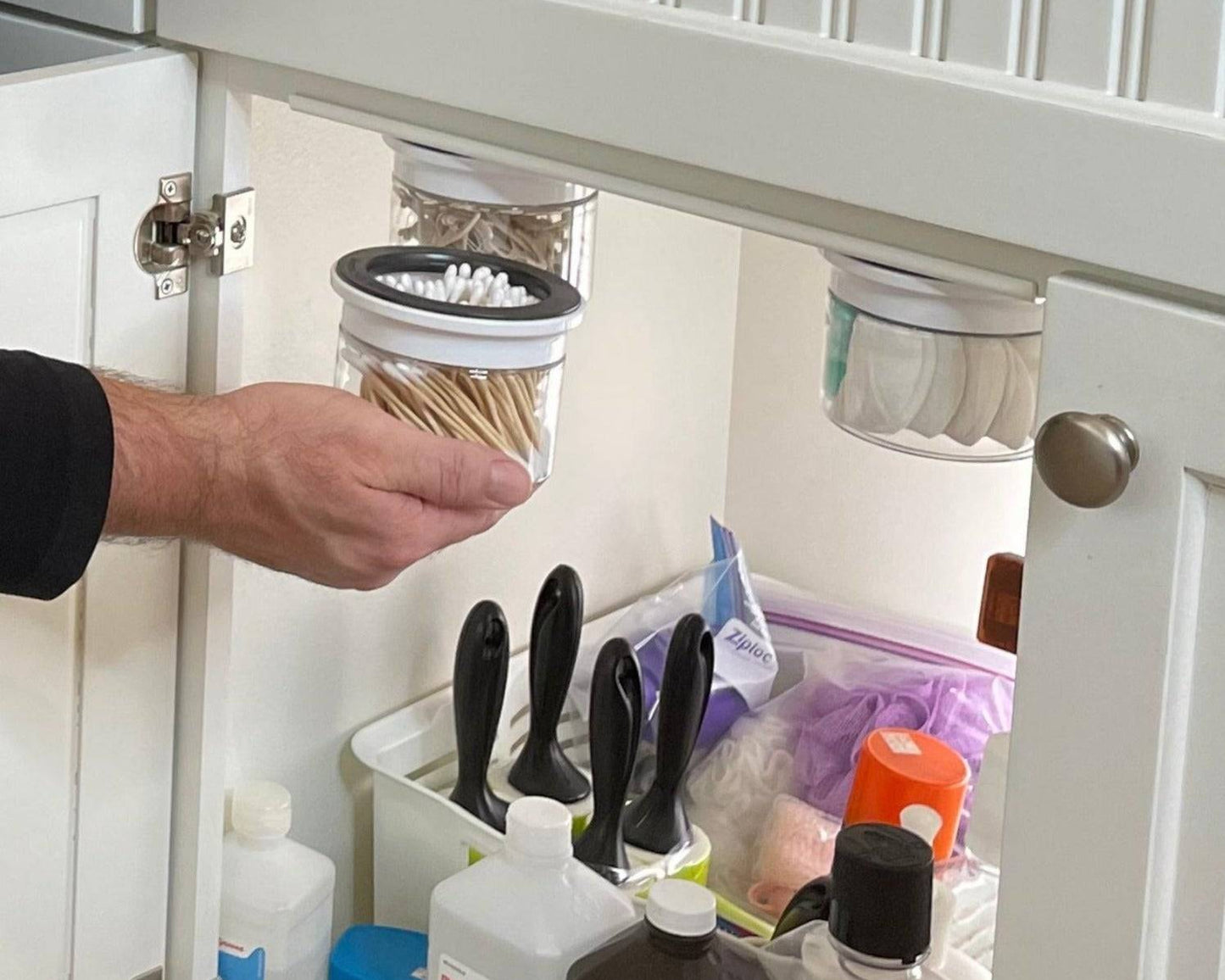 Under sink bathroom storage canisters for Q-tips and cotton swabs in a labeled, space-saving organizer. Ideal for decluttering cabinets.