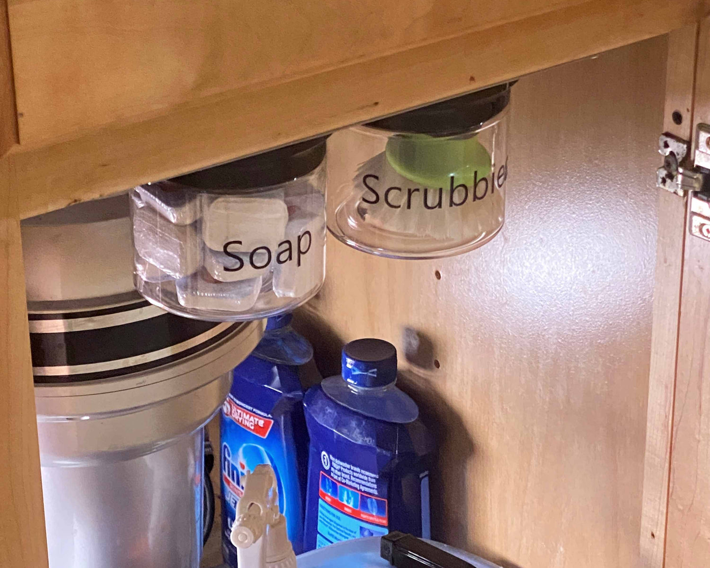 Mounted under sink organizer jars labeled 'Soap' and 'Scrubbies' in break room cabinet, optimizing space with airtight storage containers.