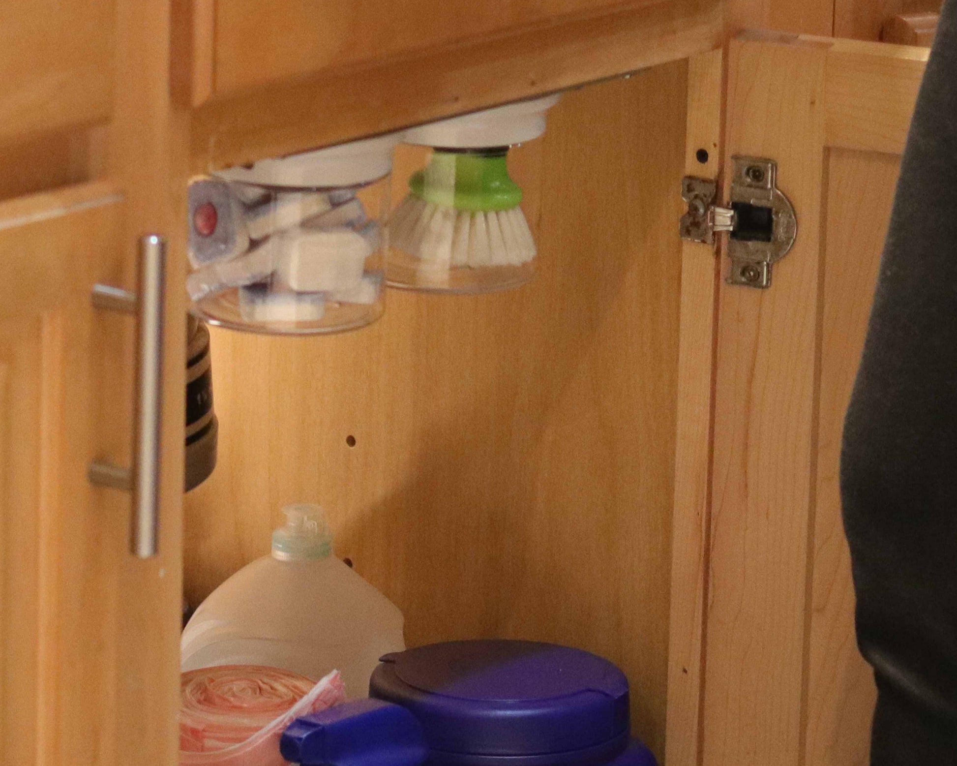 Under sink organizer jars in break room cabinet storing soap pods and scrub brush, showcasing efficient use of vertical cabinet space.