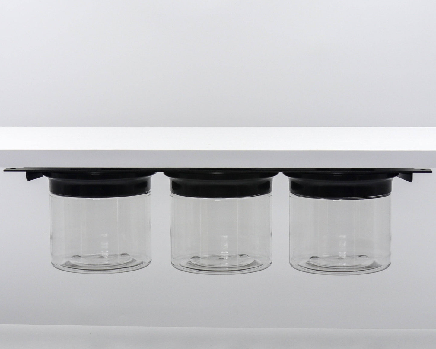 Three clear canisters with black lids mounted under shelf. Ideal for bathroom storage of cotton rounds, flossers, and Q-tips.