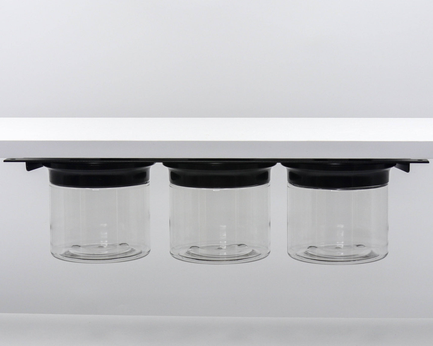 Three clear canisters with black lids mounted under shelf. Ideal for under sink bathroom storage and decluttering.