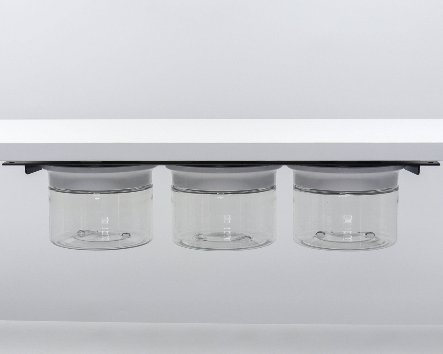 Three clear canisters with white lids mounted under shelf. Sleek and modern under sink bathroom storage solution.
