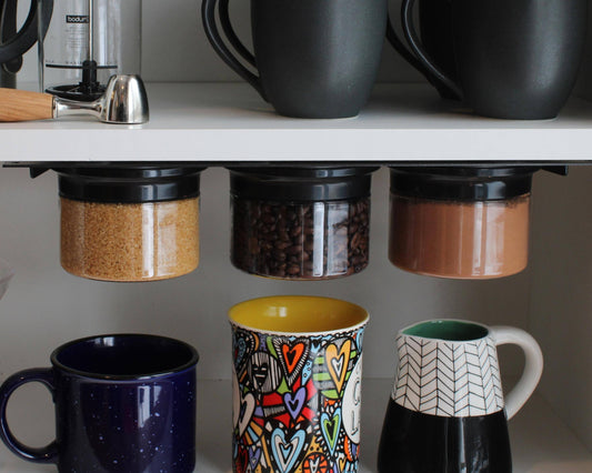 Under cabinet storage organizer with airtight jars holding sugar, coffee, and cocoa. Space-saving kitchen solution with mugs below.