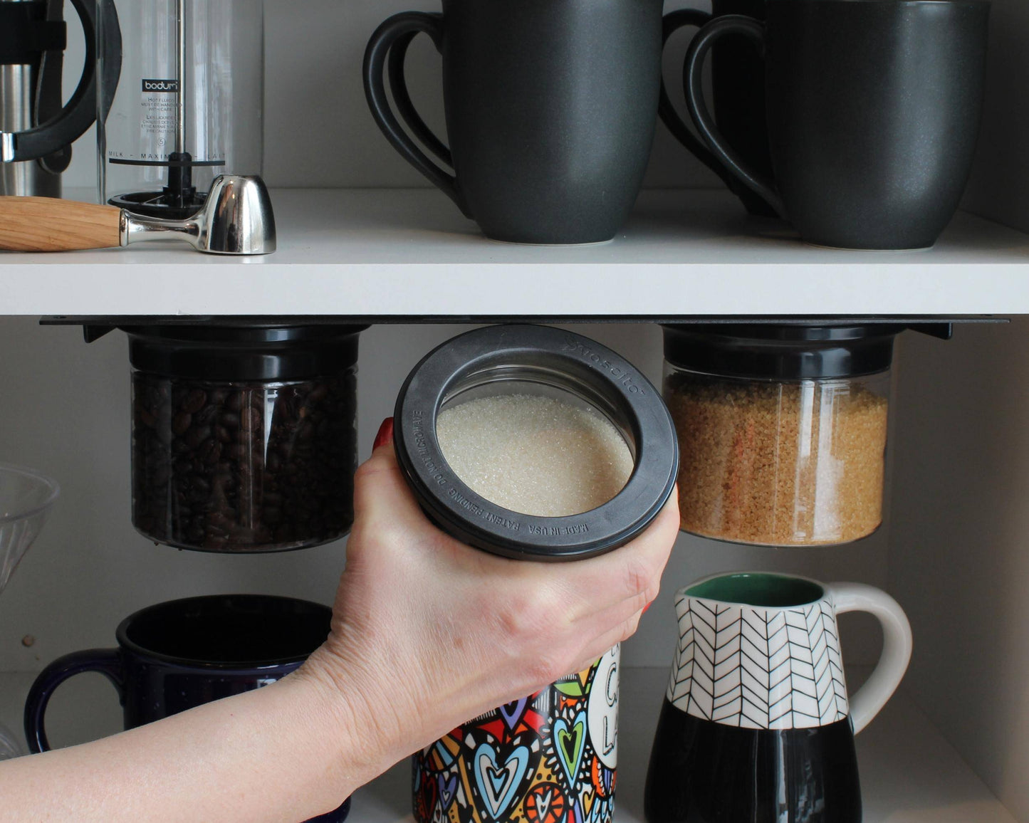 Under cabinet storage organizer with airtight jars for sugar, coffee, and spices. Space-saving kitchen solution ideal for mugs and small kitchens.