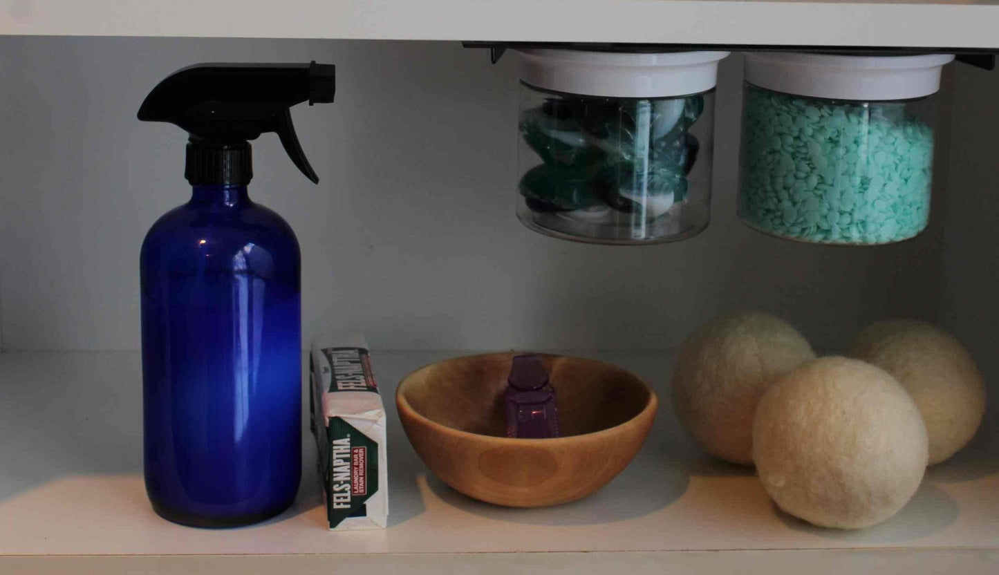 Under sink shelf with Laundry Containers Organizer jars storing detergent and scent beads, alongside laundry essentials like wool dryer balls and spray bottle.