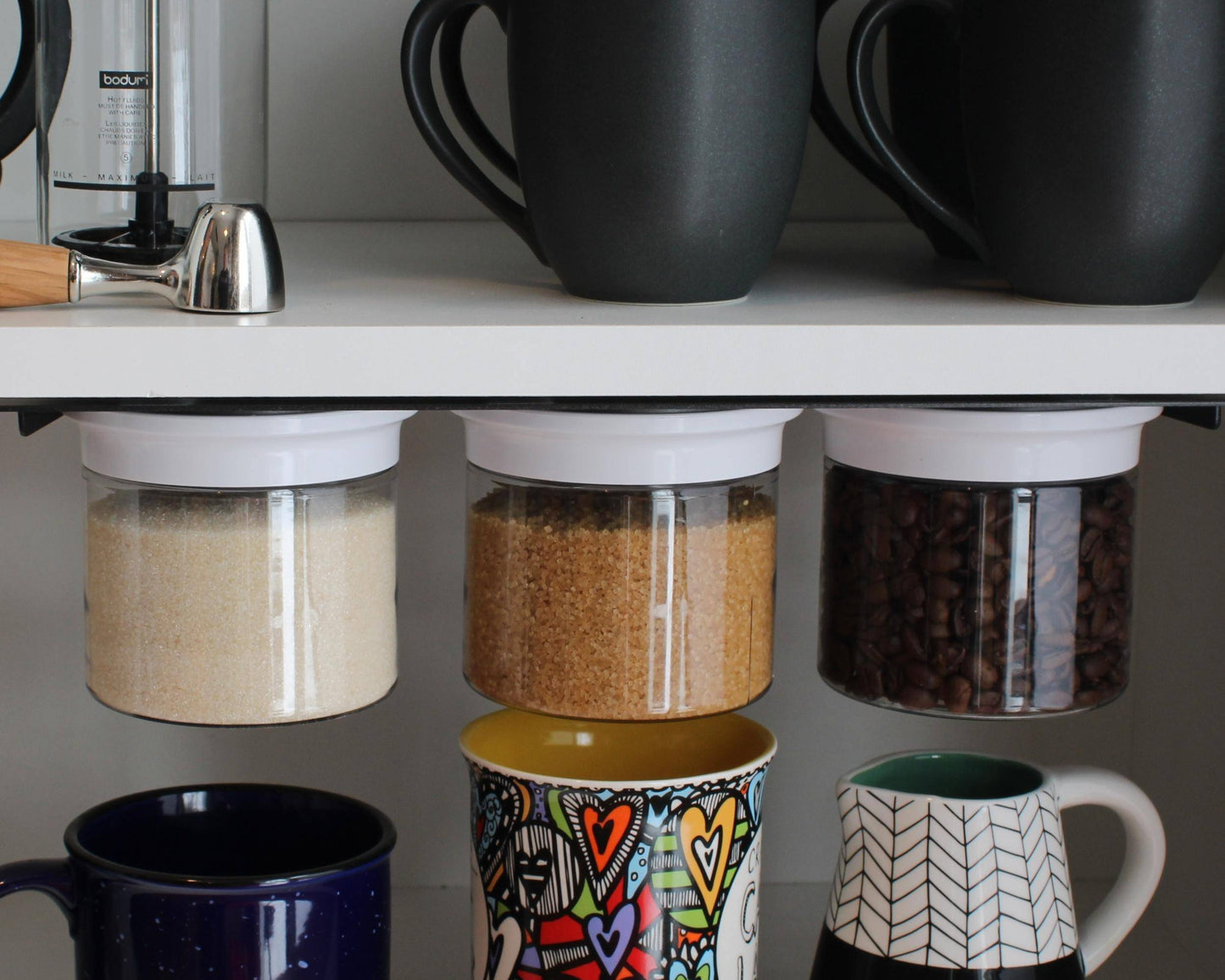 White lid airtight jars under cabinet storing sugar, brown sugar, and coffee. Stylish and functional kitchen storage solution.