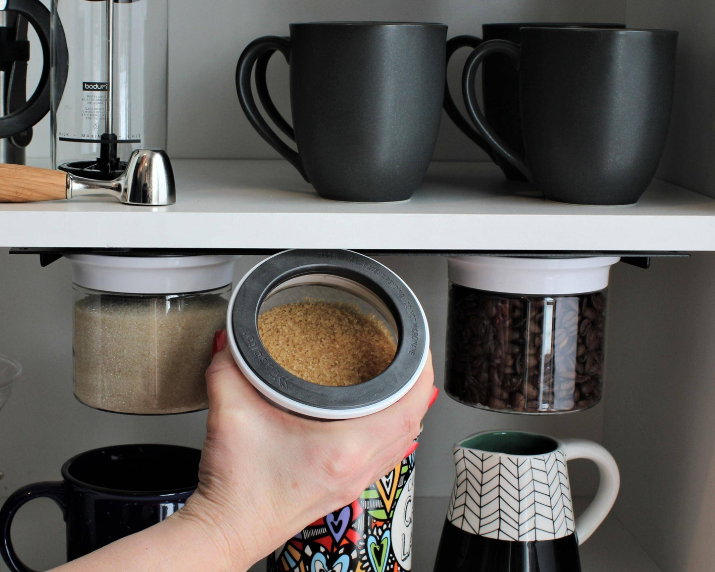 Hand accessing brown sugar from airtight jar in under cabinet organizer. Space-saving kitchen tool for spices and dry goods.