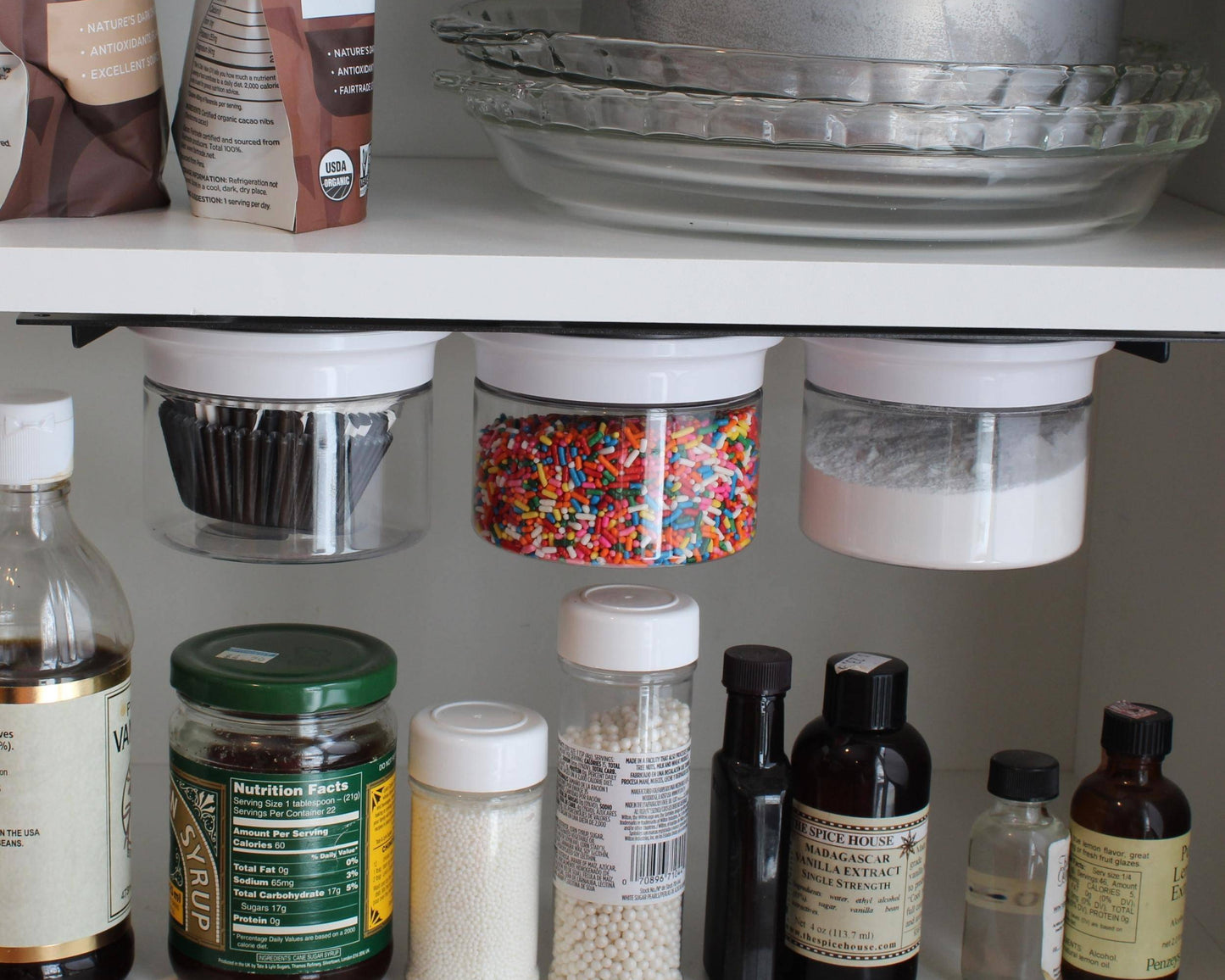 Under cabinet storage jars filled with baking supplies like sprinkles and flour. Great for organizing kitchen or pantry essentials.