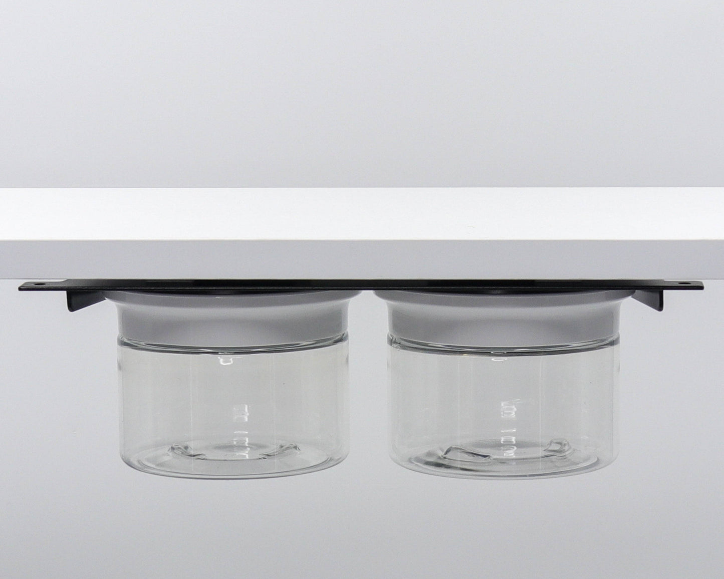 Two clear canisters with white lids mounted under shelf. Minimalist bathroom storage solution for cotton rounds and Q-tips.