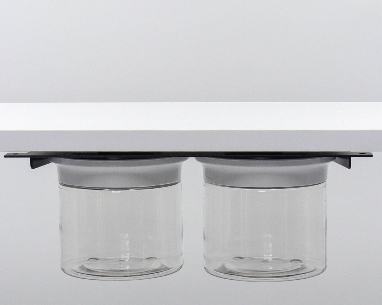 Dual canisters with white lids mounted under shelf. Efficient under sink storage for bathroom accessories.