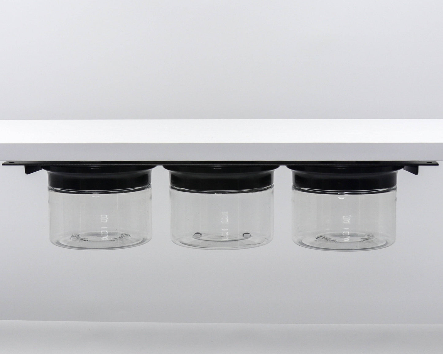 Three clear canisters with black lids mounted under shelf. Perfect for organizing bathroom items like flossers and cotton balls.