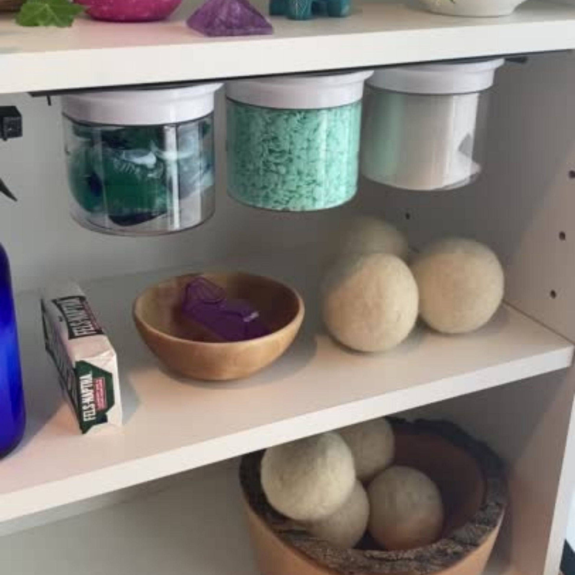 Laundry Room Storage Jars - Space Saving Canisters mounted under a shelf, storing scent beads, dryer sheets, and laundry pods in a compact dual shelf setup.