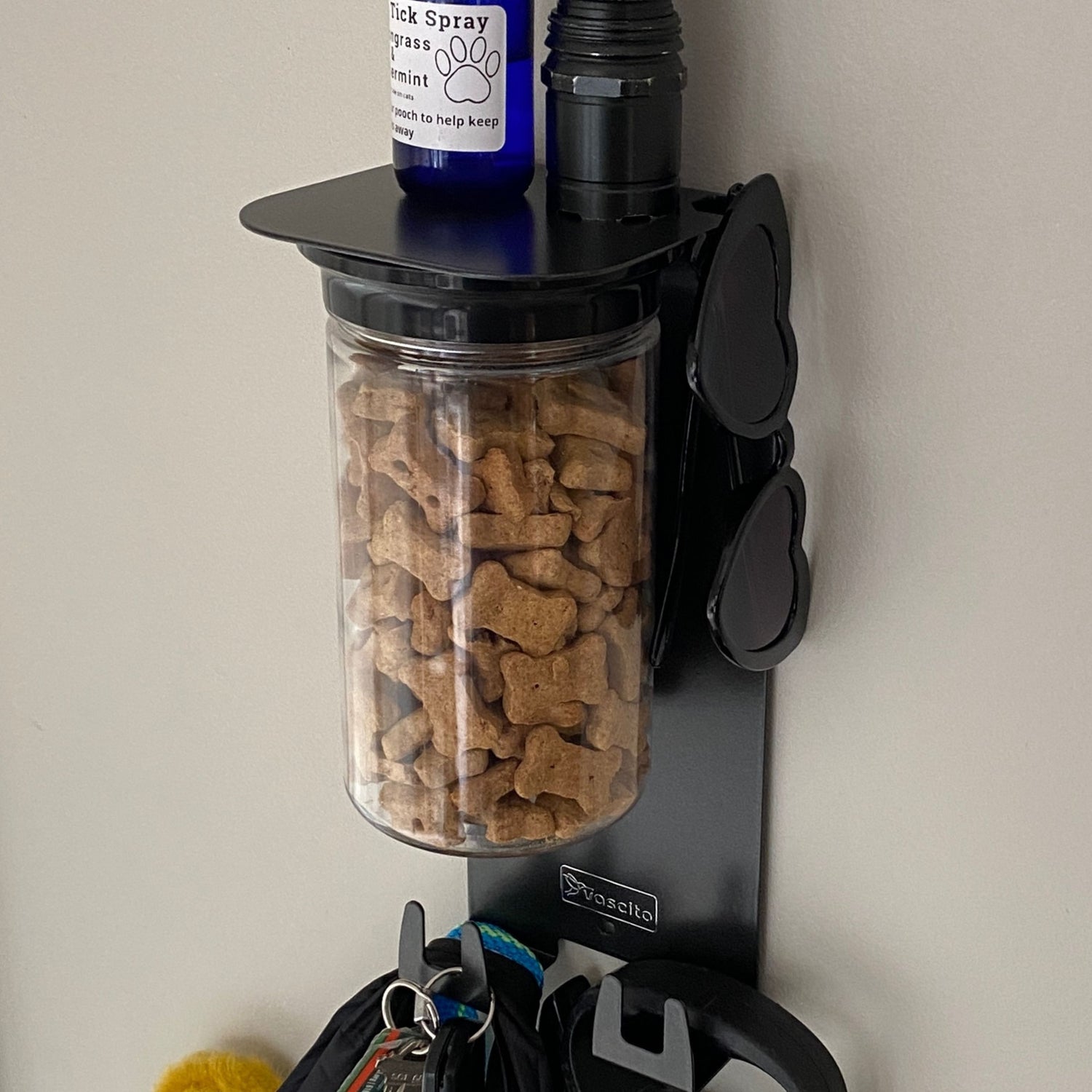 Wall-mounted dog biscuit jar with bone-shaped treats inside.