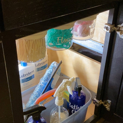Under Sink/Under Shelf Organizer, Stainless POS jars labeled for flossers and Q-tips mounted under cabinet for efficient bathroom storage.