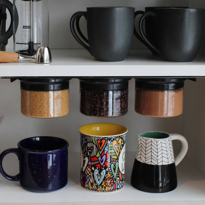 Magnetic airtight jars storing sugar, coffee beans, and cocoa powder under a kitchen shelf, optimizing space above colorful mugs.