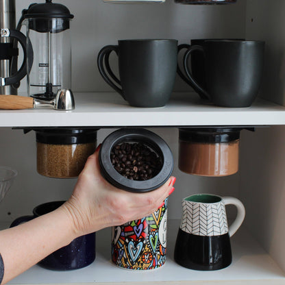 Hand removing magnetic airtight jar filled with coffee beans from under-shelf storage, showcasing space-saving kitchen organizer solution.