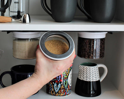 Hand removing brown sugar from a white magnetic airtight jar under a kitchen shelf, showing accessible and space-saving storage.