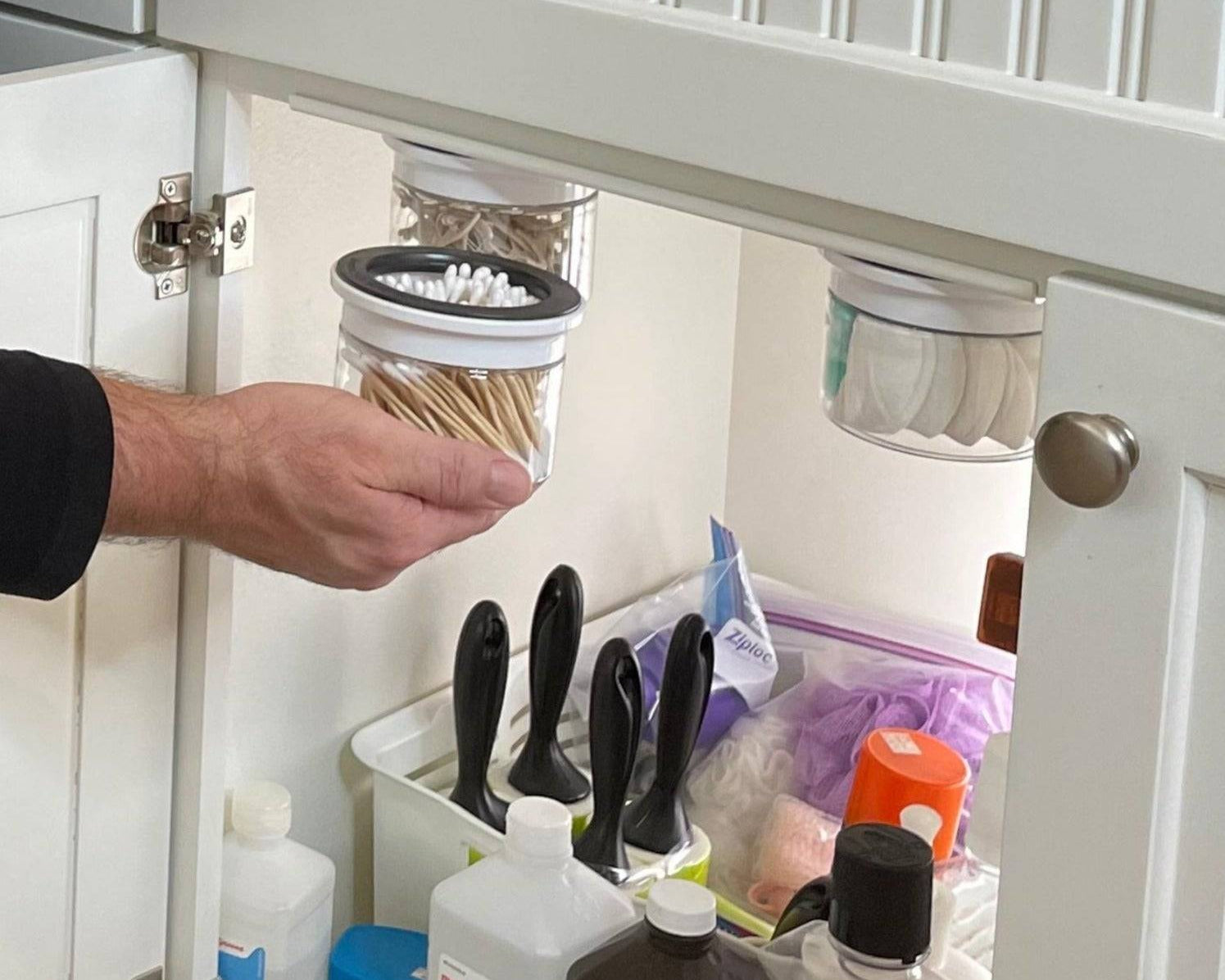 Under sink bathroom storage canisters for Q-tips and cotton swabs in a labeled, space-saving organizer. Ideal for decluttering cabinets.