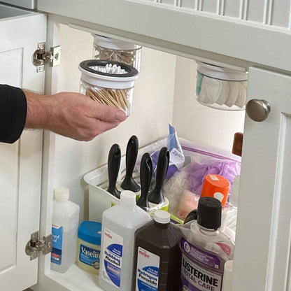 Under sink bathroom storage canisters for Q-tips and cotton swabs in a labeled, space-saving organizer. Ideal for decluttering cabinets.