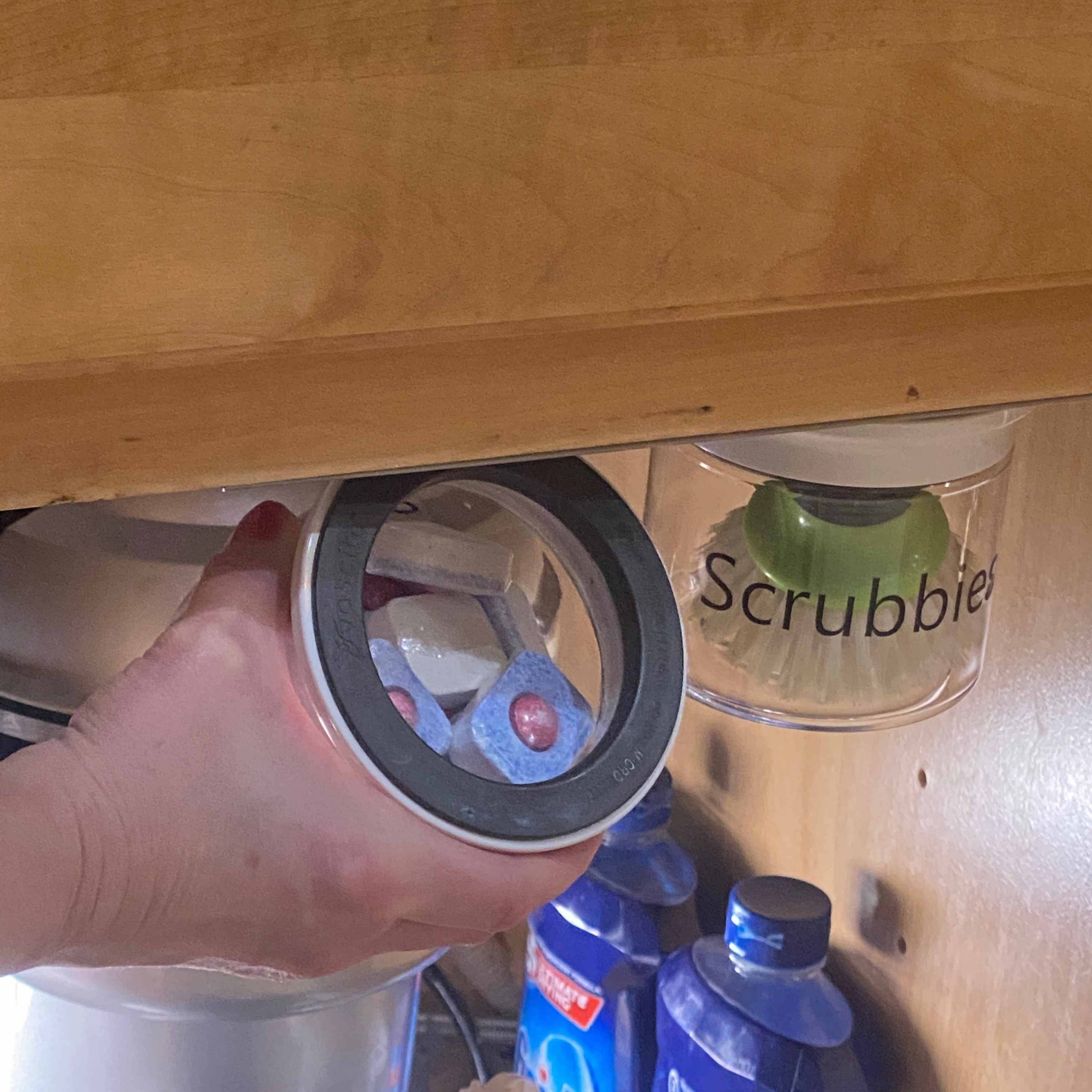 Hand removing airtight jar labeled Soap from magnetic under sink organizer, showcasing easy access and space-saving kitchen storage.