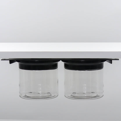 Dual canister set with black lids mounted under shelf. Space-saving bathroom organizer for small essentials.